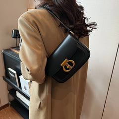 Person wearing a black handbag with a gold clasp in an indoor setting