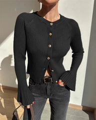 Person wearing a black ribbed cardigan with gold buttons against a neutral wall.