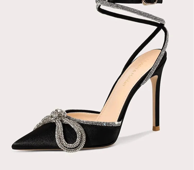 Black high-heeled shoe with decorative strap on a white background