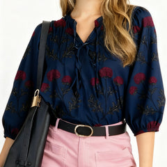 Woman wearing a navy blouse with red floral patterns and pink pants, holding a black bag.