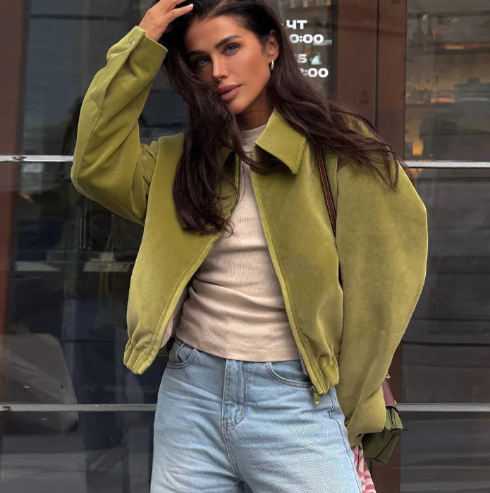 A woman wearing a green jacket and light blue jeans standing in front of a glass door