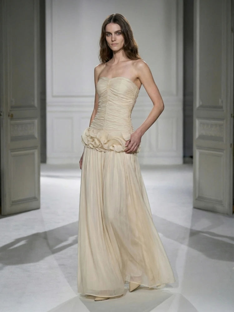 Model wearing a strapless, ruched gown with a flowing skirt on a runway.