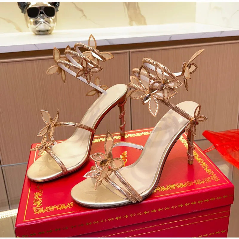 Gold high-heeled sandals with floral designs on a red box.