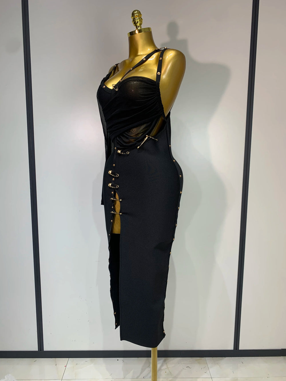 Black dress with gold accents on a mannequin against a plain background