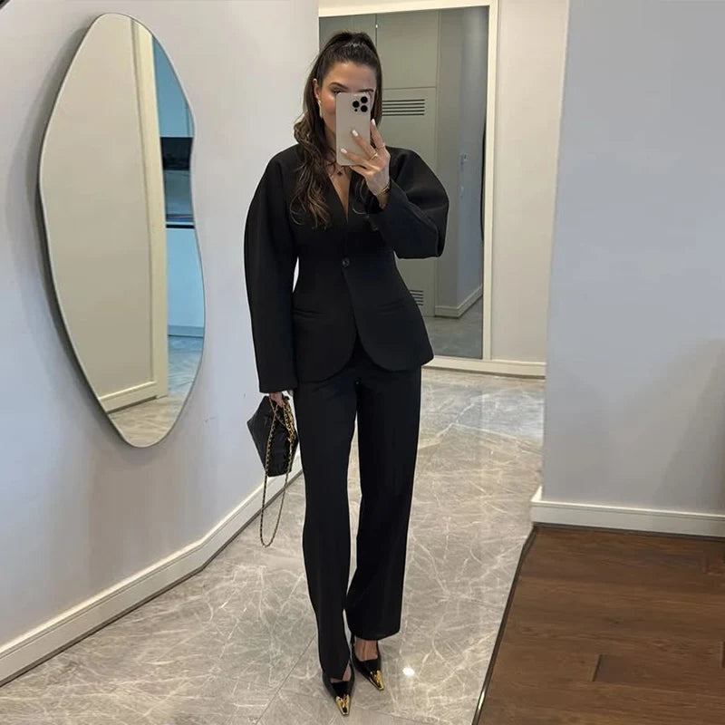 Woman taking a mirror selfie wearing a black suit in a room with a large round mirror.