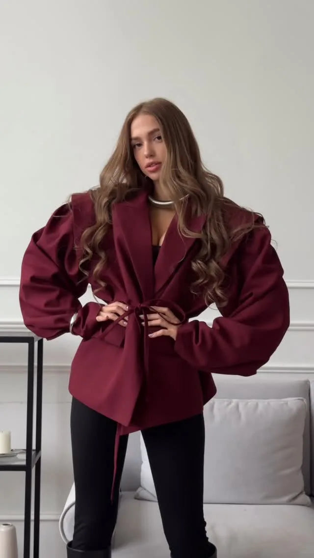Woman wearing a burgundy coat in a minimalistic room.