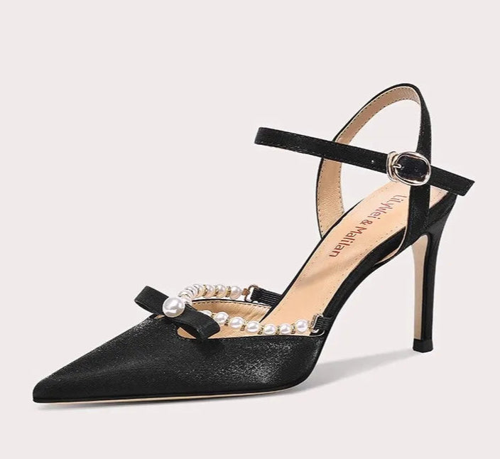 Black high-heeled shoe with pearl embellishments on a light gray background