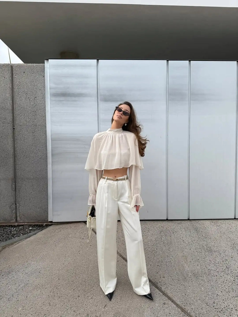 Woman in a white outfit standing in front of a modern building.