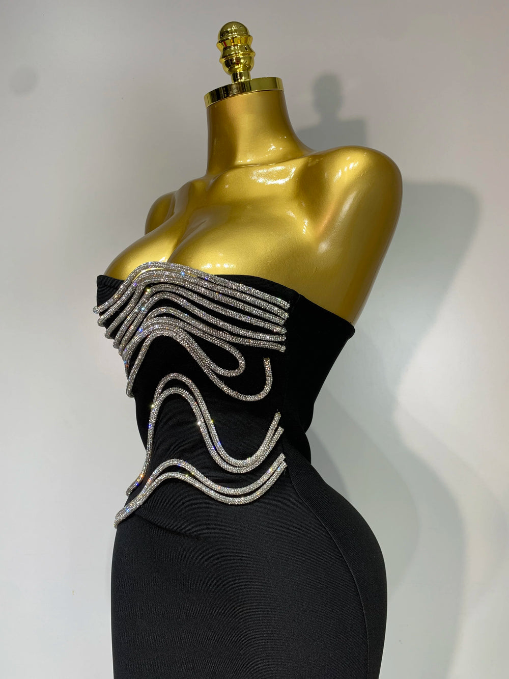 Black evening gown with silver embellishments on a gold mannequin against a white background