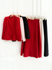 Red blazer, pink blouse, black top, and red skirt hanging on a rack against a white background