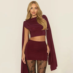 Woman wearing a burgundy outfit with a cape against a plain background
