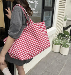 Person holding a red and white checkered bag outdoors near a building entrance.