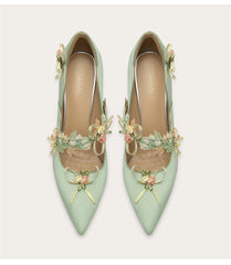 Pair of light green high heels with floral embellishments on a white background