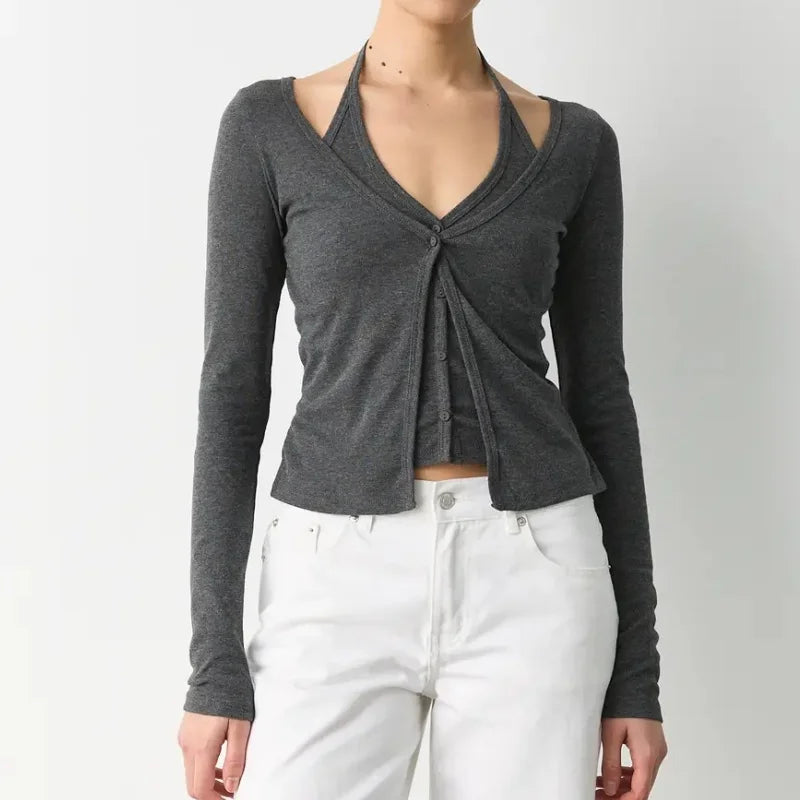 Person wearing a gray long-sleeve top with a knot detail and white pants on a plain background