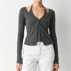 Person wearing a gray long-sleeve top with a knot detail and white pants on a plain background