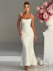 Woman in a white lace dress standing next to a floral arrangement indoors.