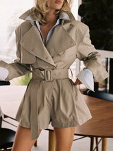 Person wearing a beige trench coat with a belt, standing indoors.