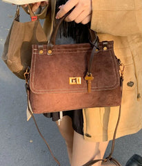 Brown leather handbag held by a person wearing a beige coat.