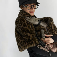 Person wearing a leopard print coat holding a dog on a white background