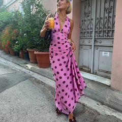 Woman in a pink polka dot dress holding a drink on a street.