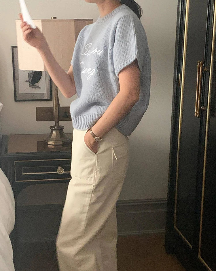 Person wearing a light blue sleeveless sweater and beige pants in a room.