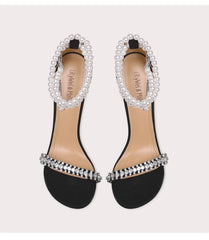 Black sandals with pearl and crystal embellishments on a light gray background