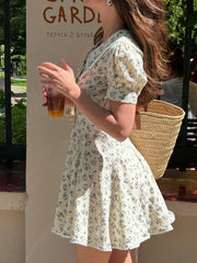 Woman in a floral dress holding a drink and a straw bag outdoors.
