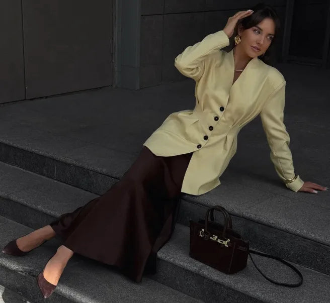 Woman in a light-colored coat sitting on steps with a black handbag beside her.