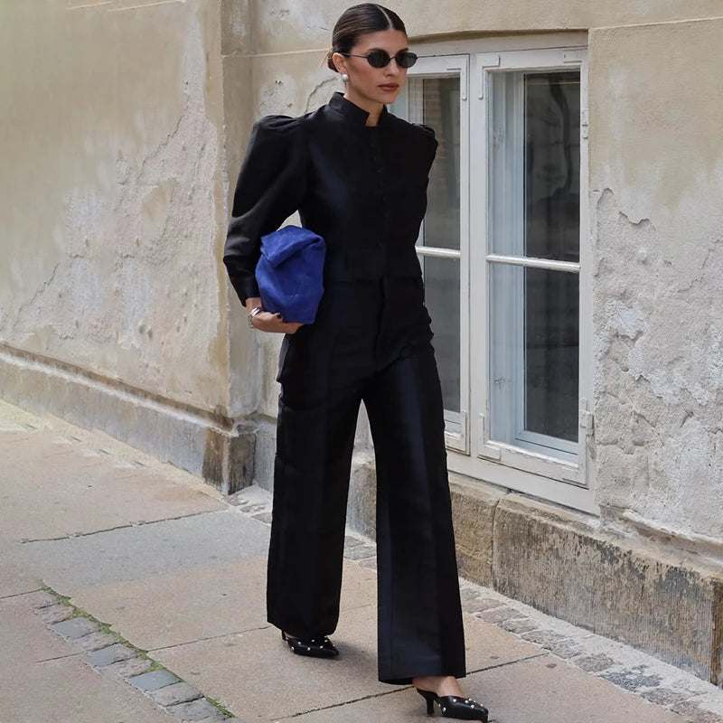 Woman in a black outfit holding a blue bag against a building background