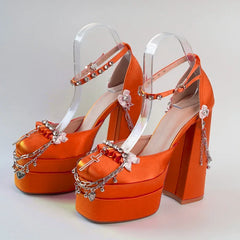 Orange high-heeled shoes with clear straps and decorative elements on a light gray background