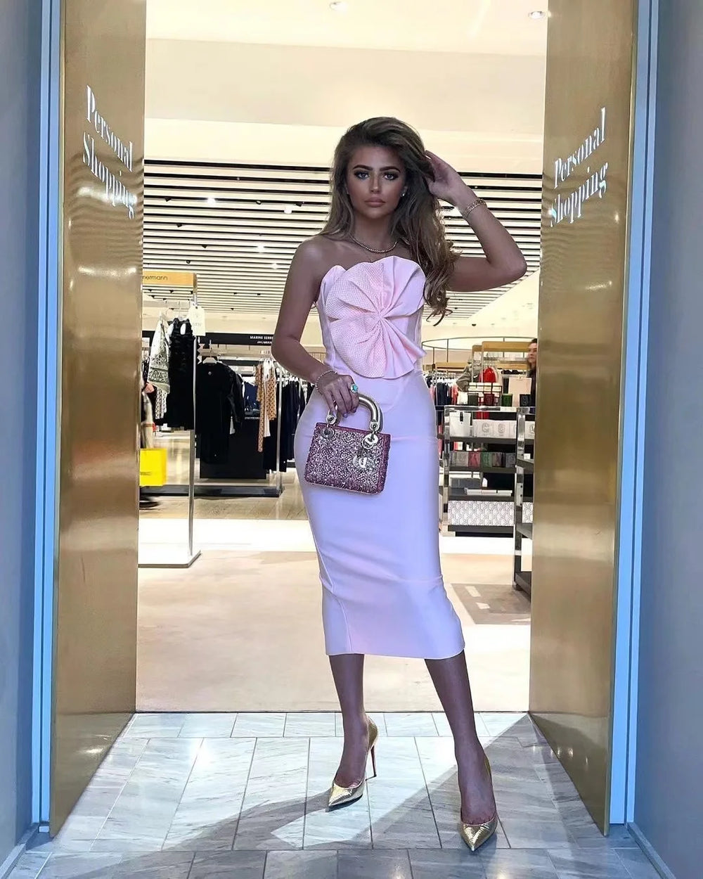 Woman in a pink dress holding a handbag in front of a store entrance