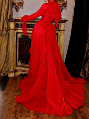 Red evening gown with long train on a wooden floor.