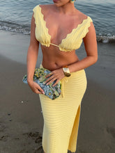Woman in a yellow crochet outfit standing on a beach.