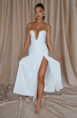 Woman wearing a white strapless dress with a high slit on a beige curtain background