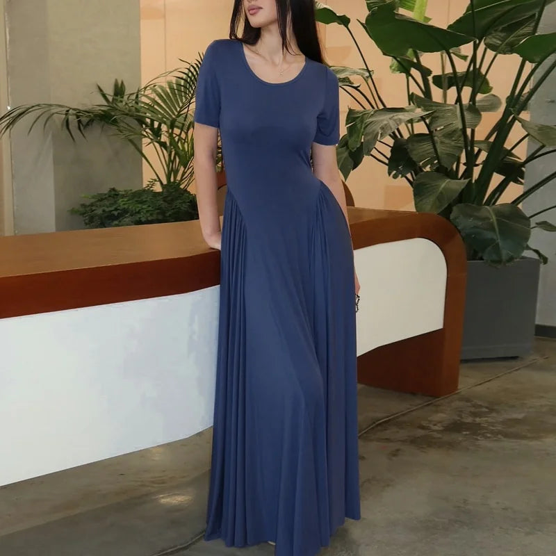 Woman in a blue dress standing in an indoor setting with plants.