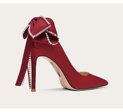 Red high-heeled shoe with a decorative bow on a light beige background