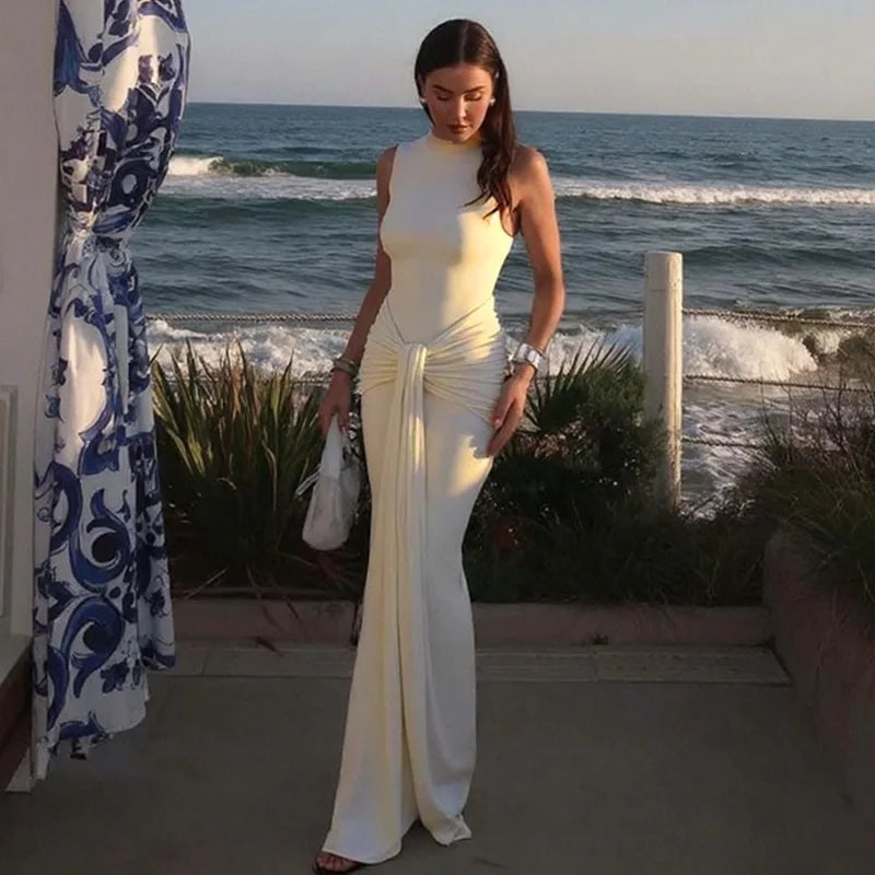 Woman in a white dress standing by the ocean with a decorative curtain on the left.