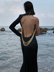 Woman in a black dress with a unique back design standing by the ocean.