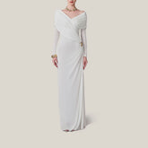 Woman wearing a white evening gown with long sleeves on a plain background