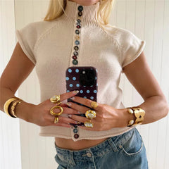Person wearing a beige turtleneck sweater with colorful buttons, holding a phone with a polka dot case.