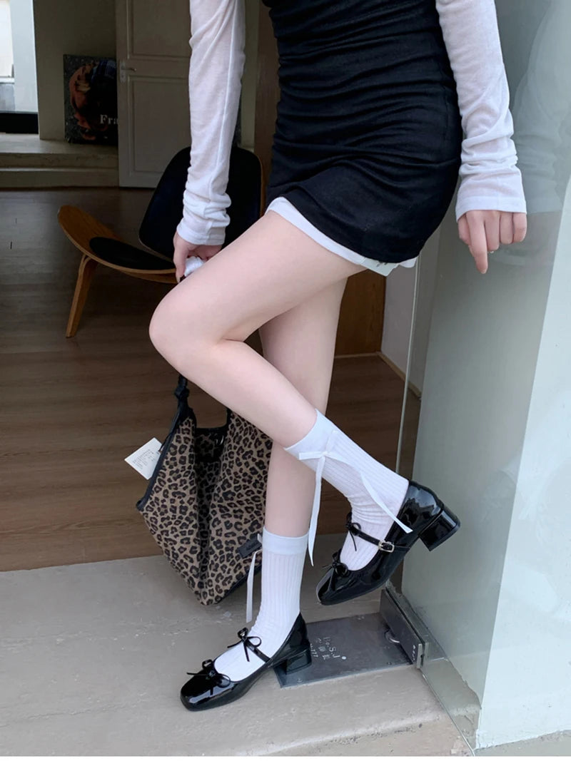 Person wearing black shoes with white bows, white socks, and a black skirt in an indoor setting.