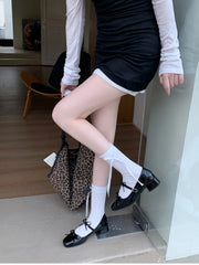 Person wearing black shoes with white bows, white socks, and a black skirt in an indoor setting.