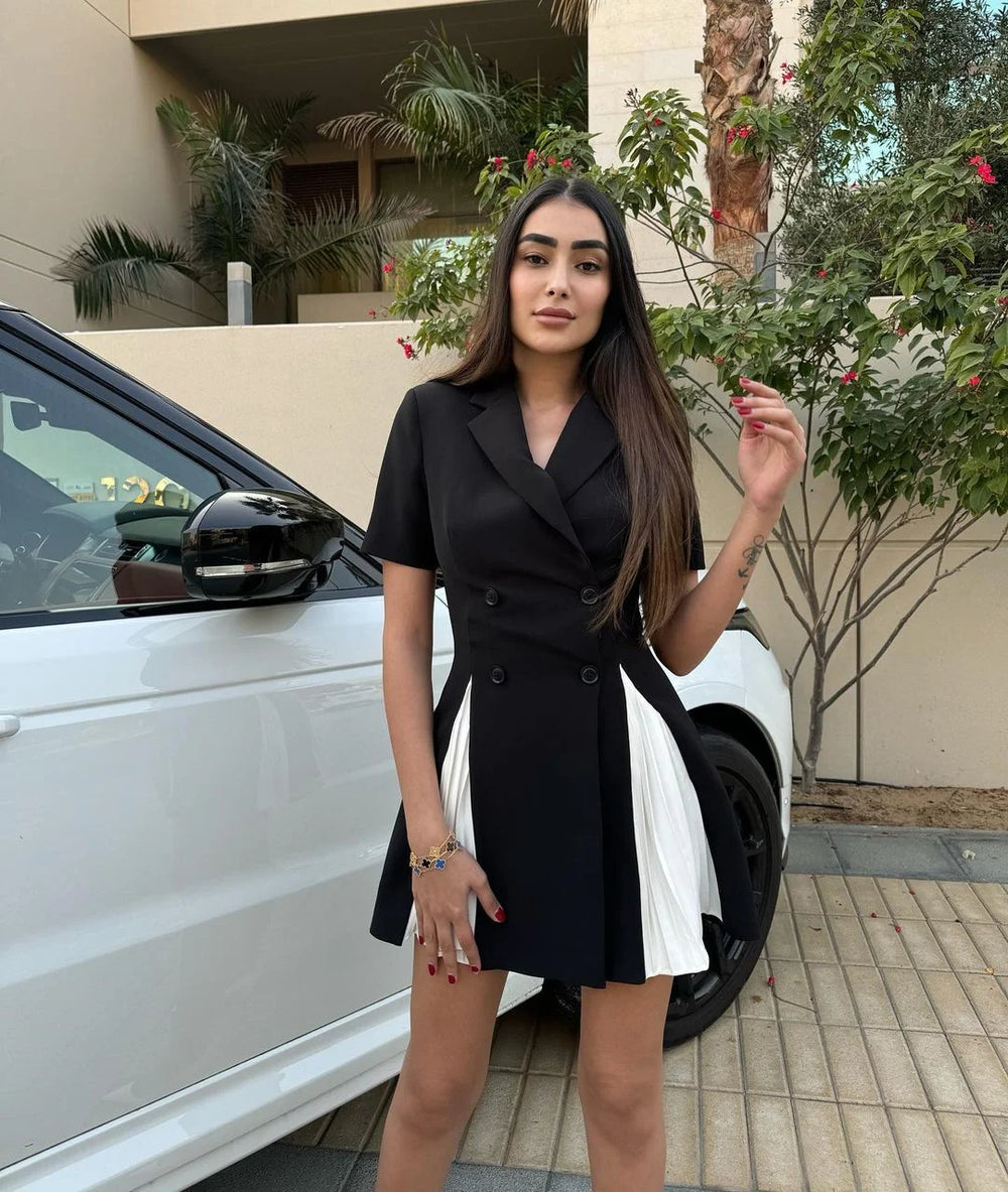 Woman in a black dress standing next to a white car with plants in the background