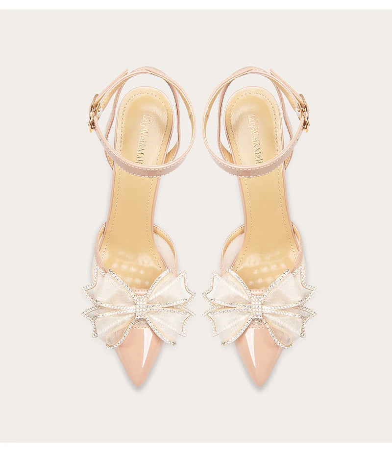 Pair of beige high-heeled shoes with bow details on a light gray background