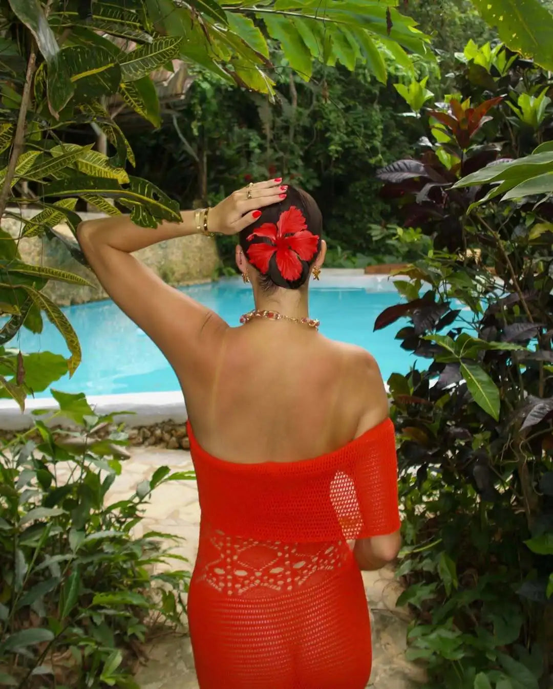 Person wearing a red dress with a floral headpiece by a poolside