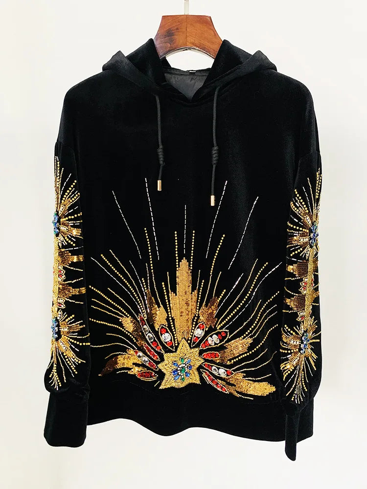 Black velvet hoodie with gold sequin and beaded sunburst embellishment, displayed on a hanger.