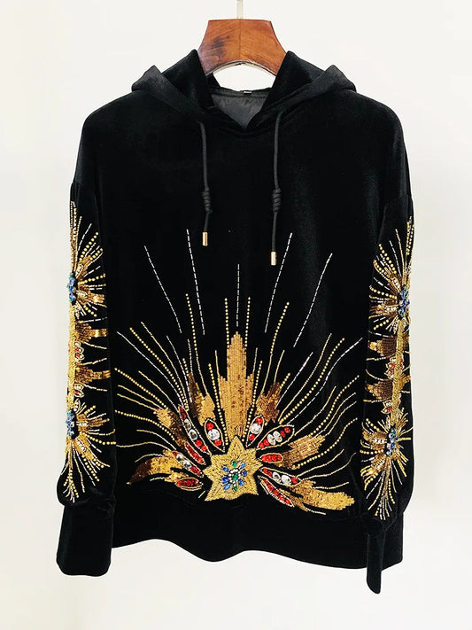 Black velvet hoodie with gold sequin and beaded sunburst embellishment, displayed on a hanger.