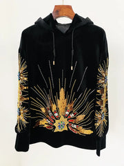 Black velvet hoodie with gold sequin and beaded sunburst embellishment, displayed on a hanger.