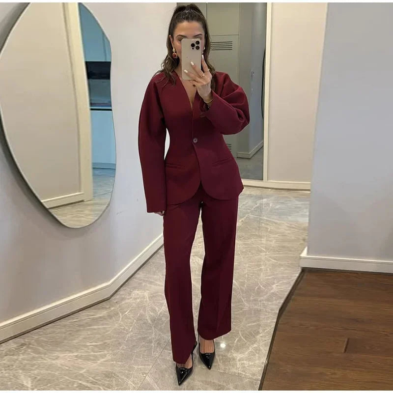 Person wearing a burgundy suit taking a mirror selfie in a room with a round mirror.