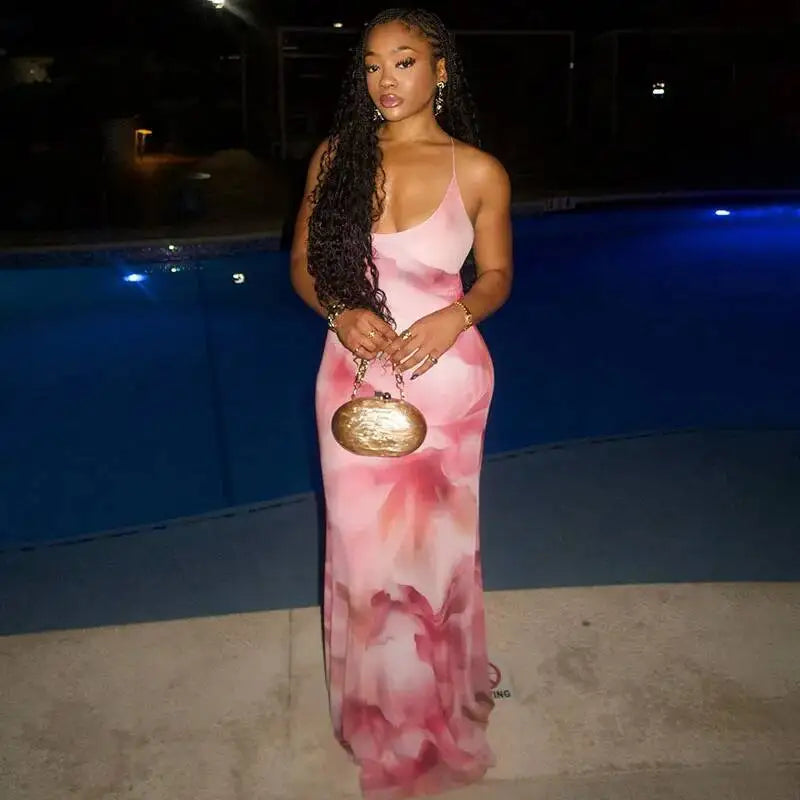 Woman in a pink floral dress holding a gold clutch by a pool at night.